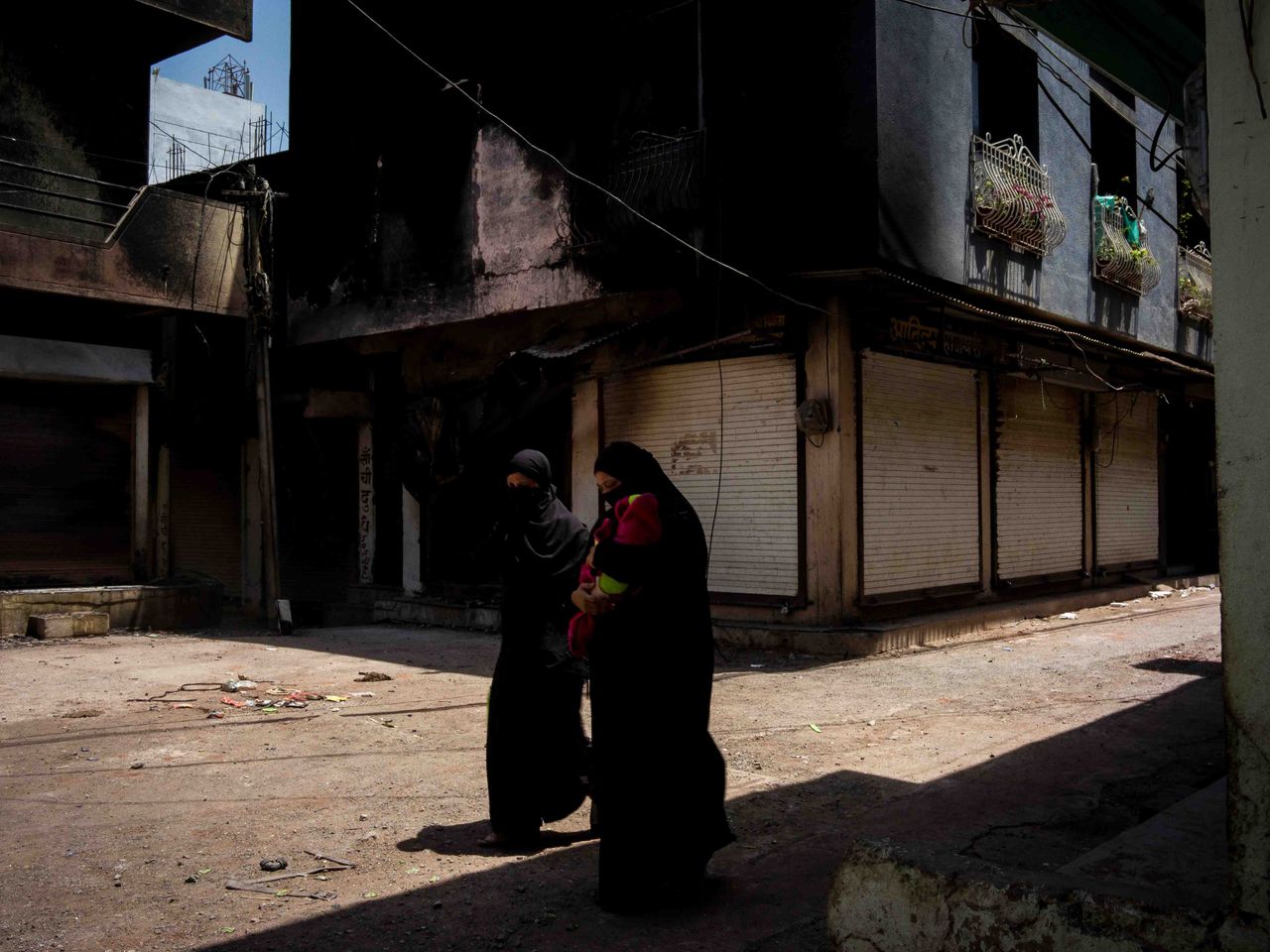 Muslim women walk past the wreckage of a house that was set alight by a mob amid communal violence in Khargone, India, on April 15, 2022. As a national campaign by right-wing groups inflames local tensions, Muslim communities are facing the harshest punishments, according to activists, analysts and retired officials.