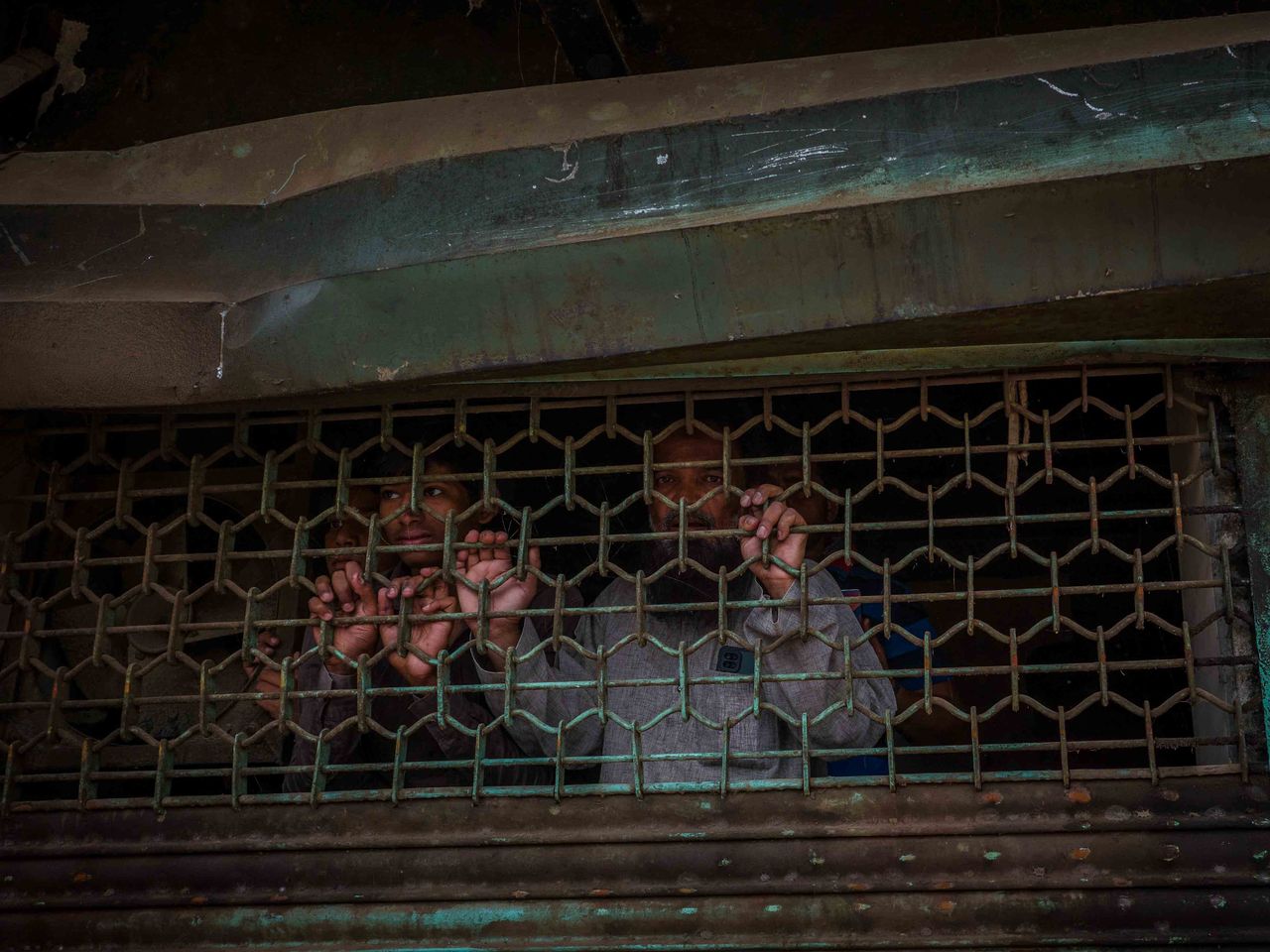 Agitated residents peep from inside a closed shutter of a damaged shop during an ongoing demolition drive against encroachment as termed by the civic authorities who used bulldozers to raze properties at a communal clash affected neighbourhood in Jahangir Puri in New Delhi on April 20, 2022. Bulldozers continued razing property for nearly two hours after India's chief justice issued an order to halt.